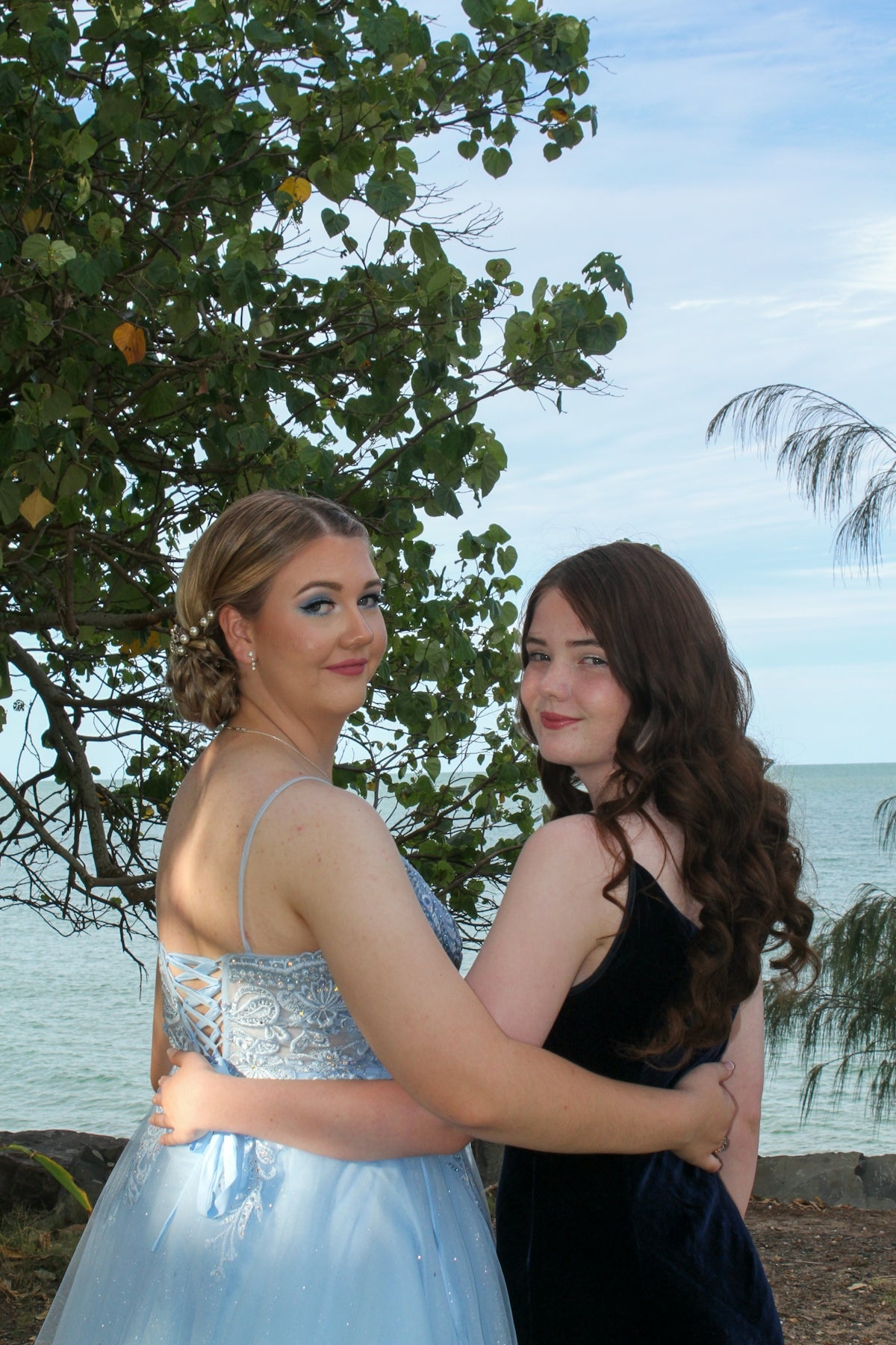 two young women standing next to each other near a tree