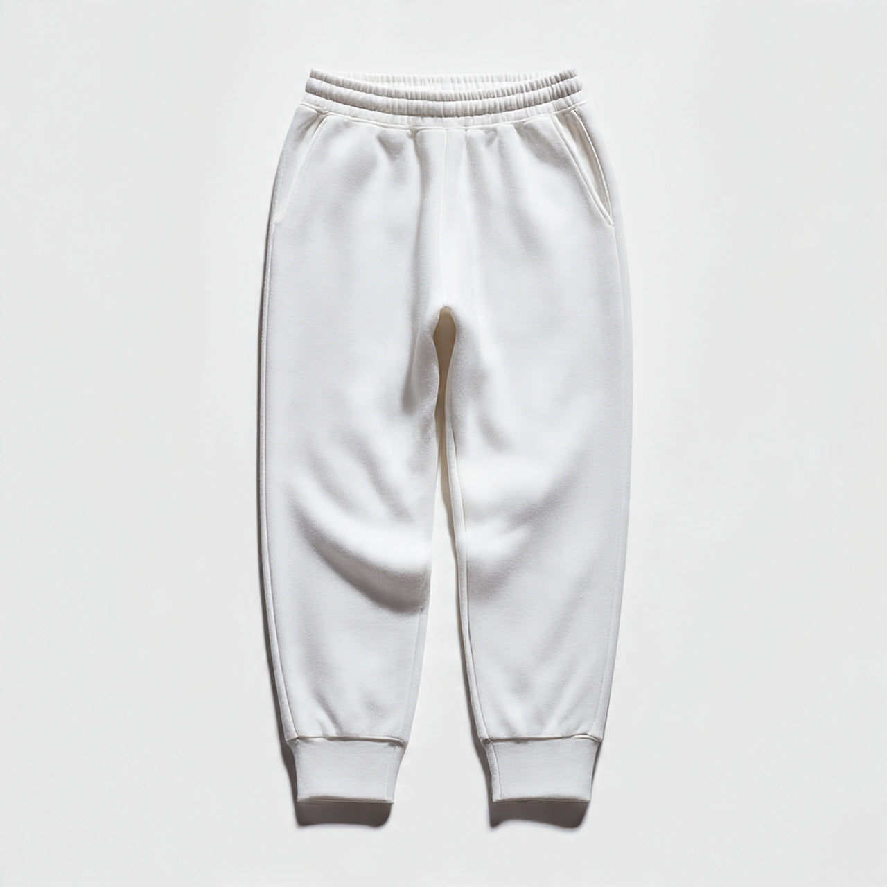 “A folded pair of women’s joggers centered on a pure white seamless background. Straight-on studio lighting with minimal shadow. No text, no logo, no model, no props.”