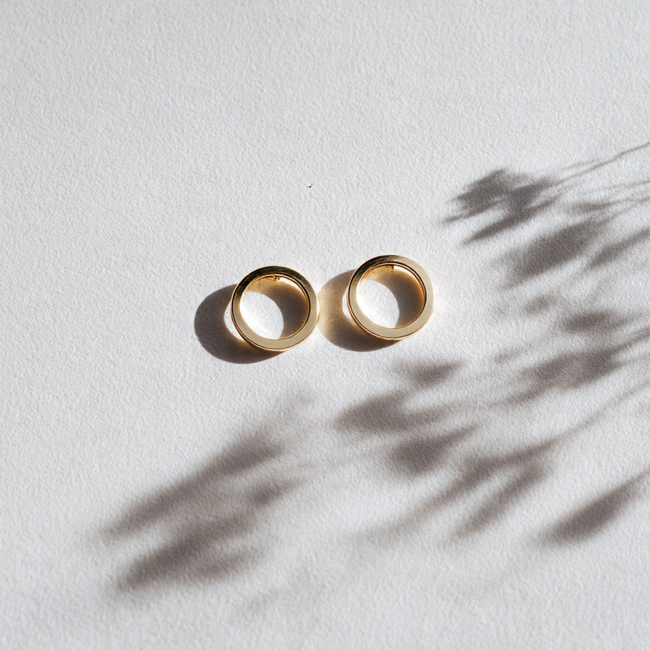 “A pair of minimalist earrings centered on a pure white seamless background. Straight-on luxury jewelry shot with soft diffused lighting and a delicate shadow. No text, no logo, no model, no props.”