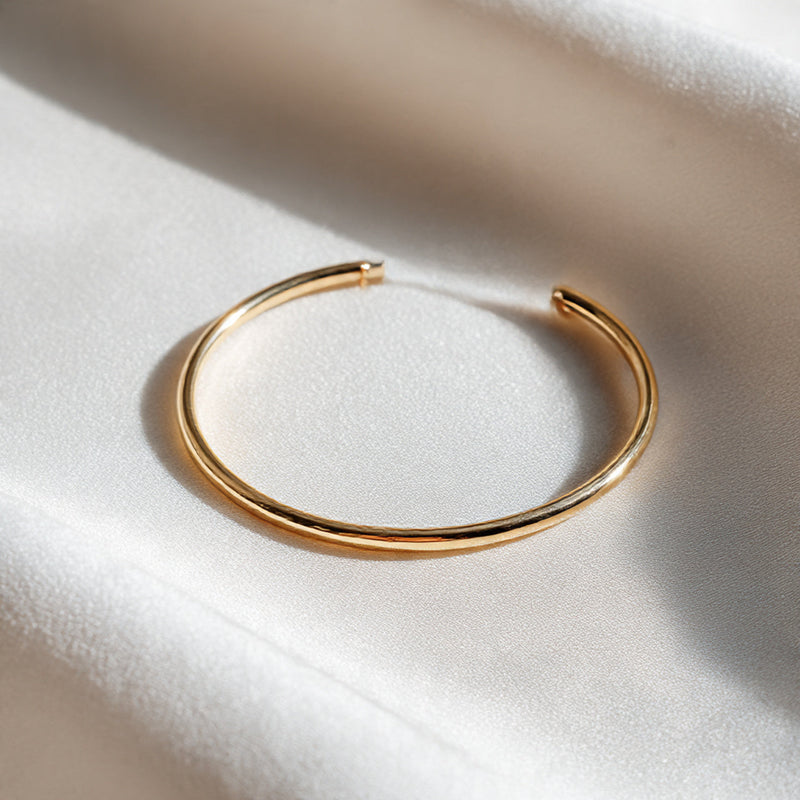 “A single minimalist gold or silver bracelet centered on a pure white seamless background. Straight-on luxury jewelry shot with soft diffused lighting and a delicate shadow. No text, no logo, no model, no props.”