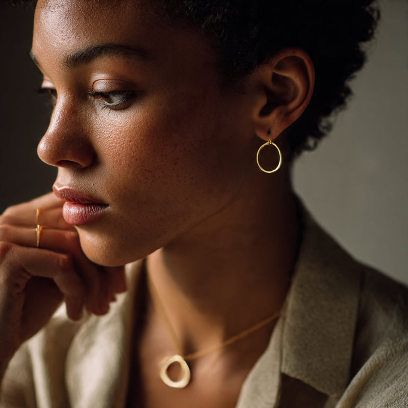 Woman wearing gold hoop earrings and a necklace with a neutral background

