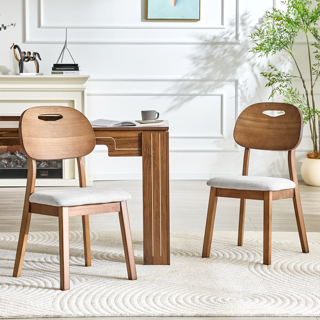 2 walnut colored solid wood dining chairs, with gray breathable fabric wrapped cushions and hollowed out backrests, suitable for home dining.
